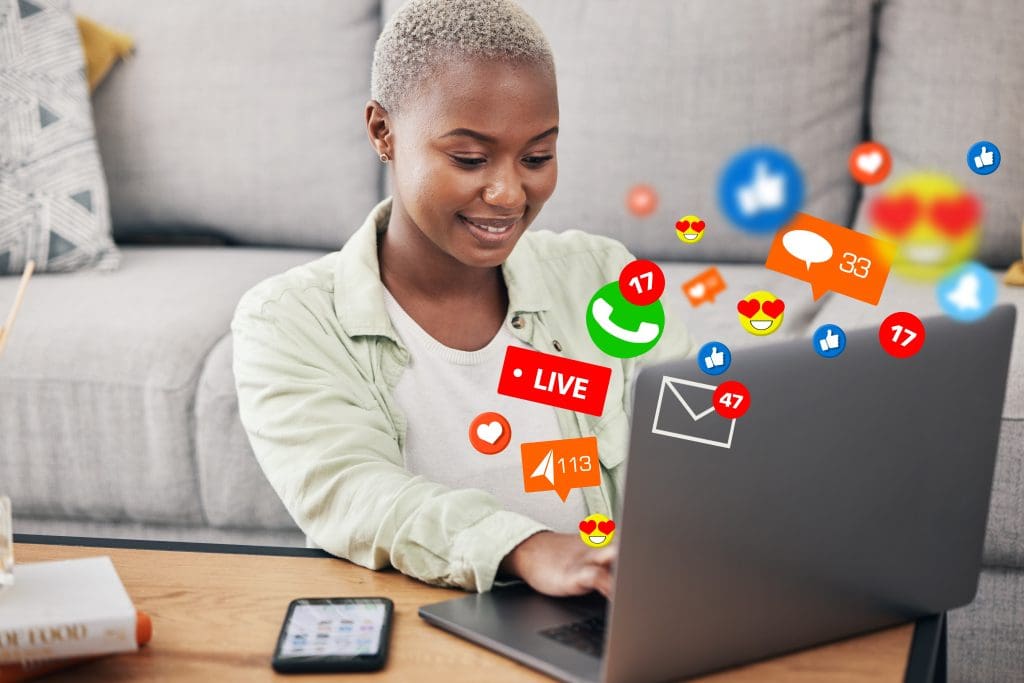 Woman, laptop and social media message icon on home floor for connection, content or platform. African influencer at computer for communication, live streaming and like or love emoji reaction overlay